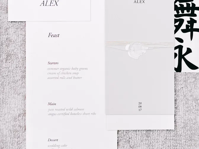 A black and white wedding menu card and place card laid out on a pale grey textured surface.
