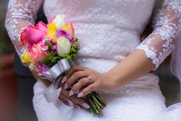 A bride in a lace dress holding a vibrant bouquet